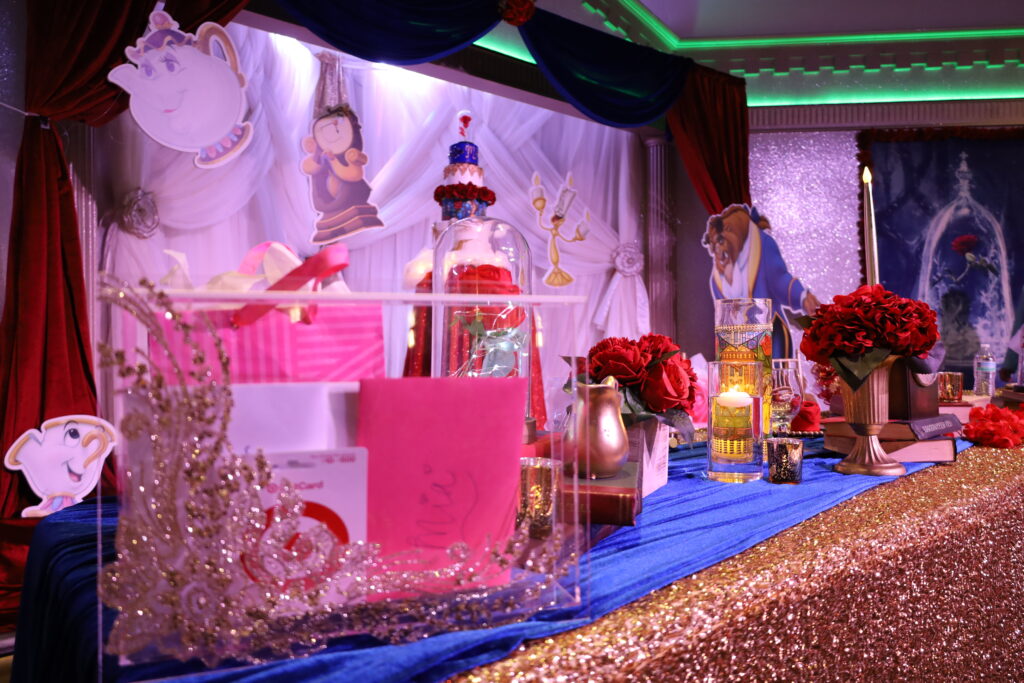 Stunning 'Beauty and the Beast' Quinceañera table setup featuring a red rose centerpiece under a glass dome, evoking the iconic story