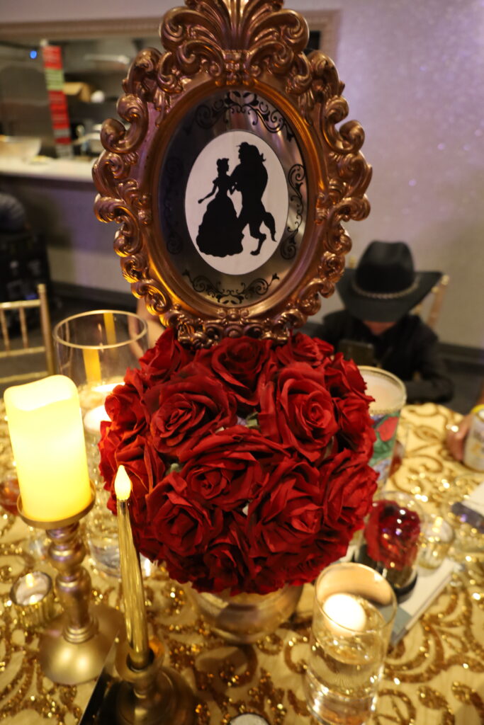 Stunning 'Beauty and the Beast' Quinceañera table setup featuring a red rose centerpiece under a glass dome, evoking the iconic story