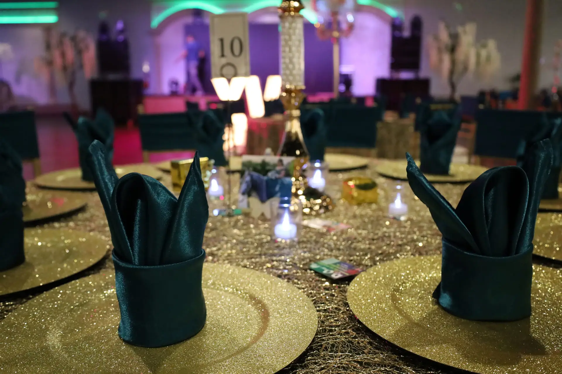 Quinceañera party in a majestic banquet hall with emerald green and gold decor, featuring opulent table settings, lush floral arrangements, and ambient lighting