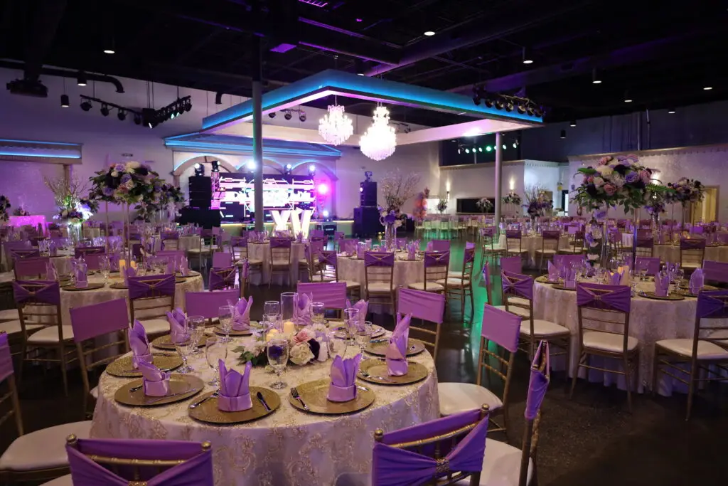 Quinceañera party in a majestic banquet hall with purple and gold decor, featuring luxurious table settings, floral arrangements, and elegant lighting