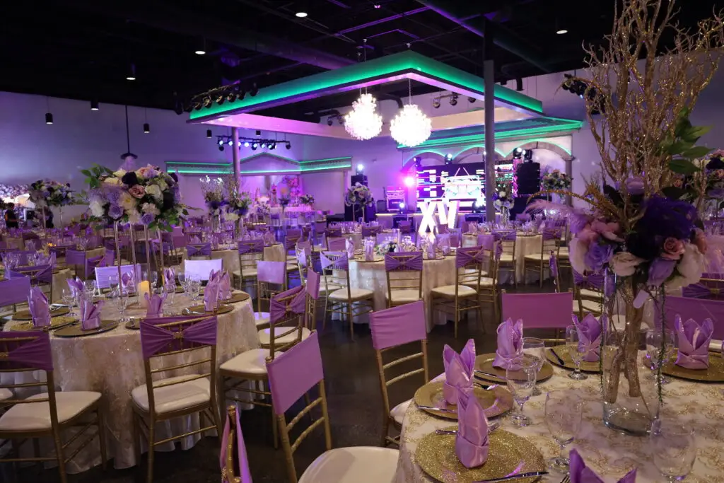 Quinceañera party in a majestic banquet hall with purple and gold decor, featuring luxurious table settings, floral arrangements, and elegant lighting