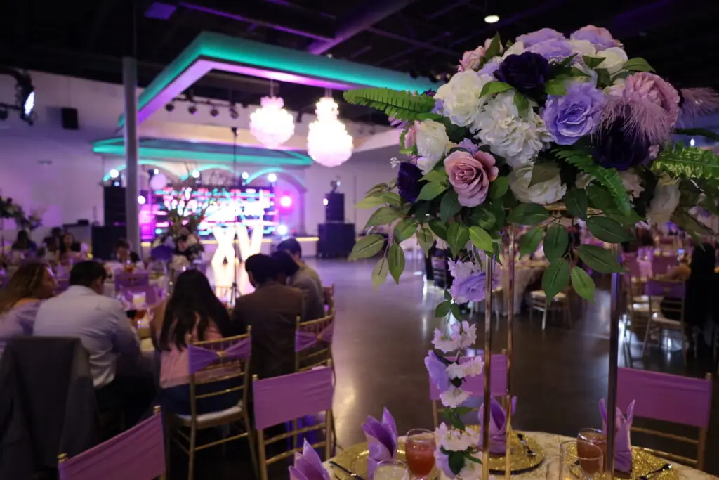 Quinceañera party in a majestic banquet hall with purple and gold decor, featuring luxurious table settings, floral arrangements, and elegant lighting