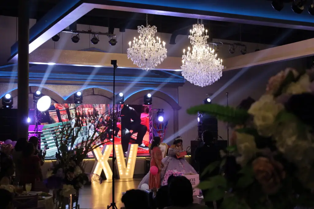 Quinceañera presentation featuring a beautifully dressed young woman in a ball gown, surrounded by elegant decorations and family members