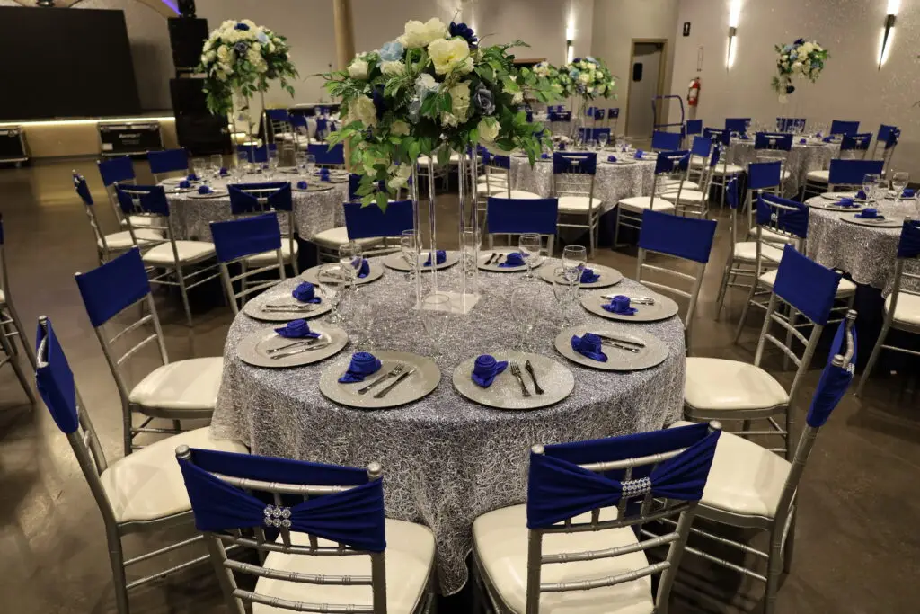 Quinceañera party in a majestic banquet hall with blue and silver decor, featuring elegant table settings, shimmering accents, and dazzling lighting