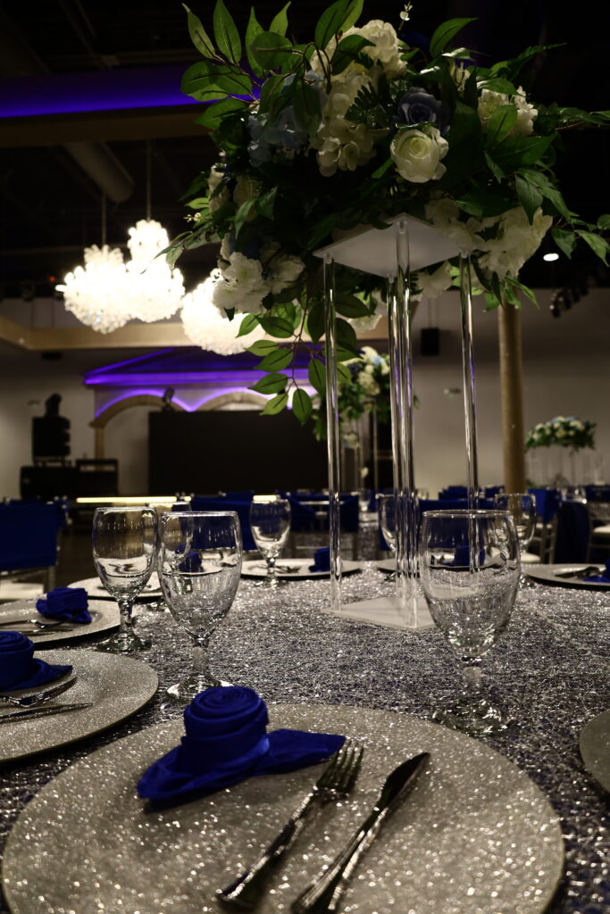 Quinceañera party in a majestic banquet hall with blue and silver decor, featuring elegant table settings, shimmering accents, and dazzling lighting