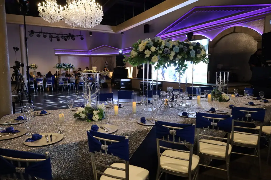 Quinceañera party in a majestic banquet hall with blue and silver decor, featuring elegant table settings, shimmering accents, and dazzling lighting