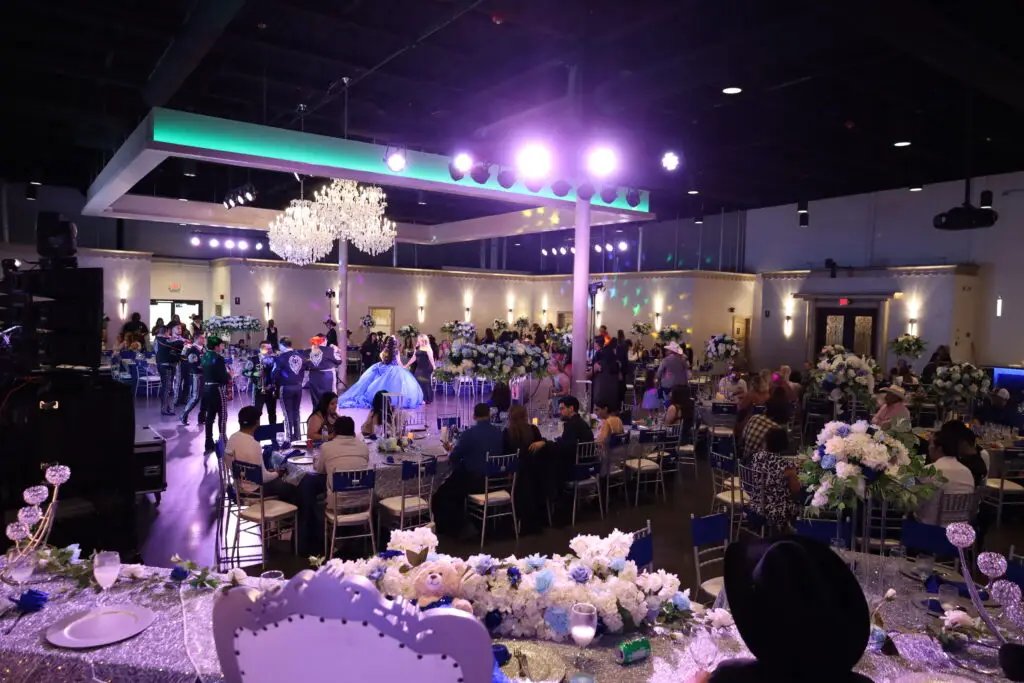 Quinceañera party in a majestic banquet hall with blue and silver decor, featuring elegant table settings, shimmering accents, and dazzling lighting