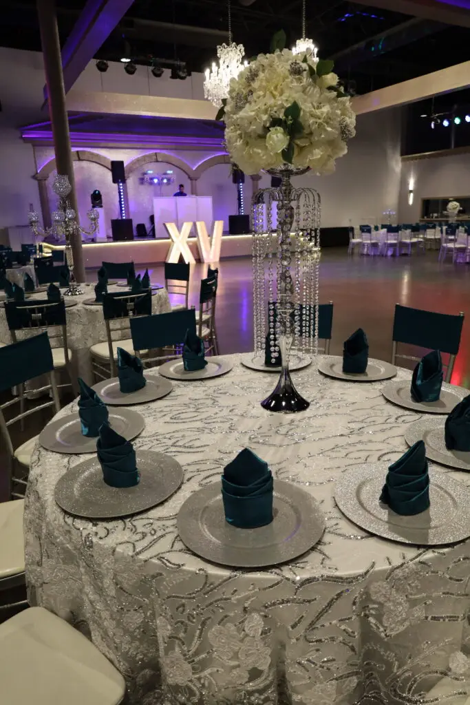 Quinceañera party in a majestic banquet hall with blue and silver decor, featuring elegant table settings, shimmering accents, and dazzling lighting