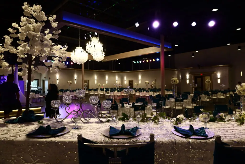 Quinceañera party in a majestic banquet hall with blue and silver decor, featuring elegant table settings, shimmering accents, and dazzling lighting